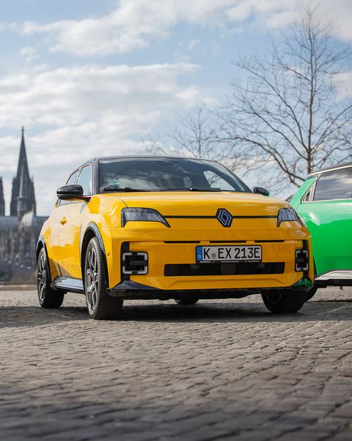 Zu sehen ist ein gelbes Auto von der Marke Renault. Dieses präsentiert sich im Sonnenschein vor dem Kölner Dom.