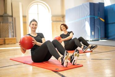 Hier siehst du zwei Frauen beim Sport mit dem Medizinball.